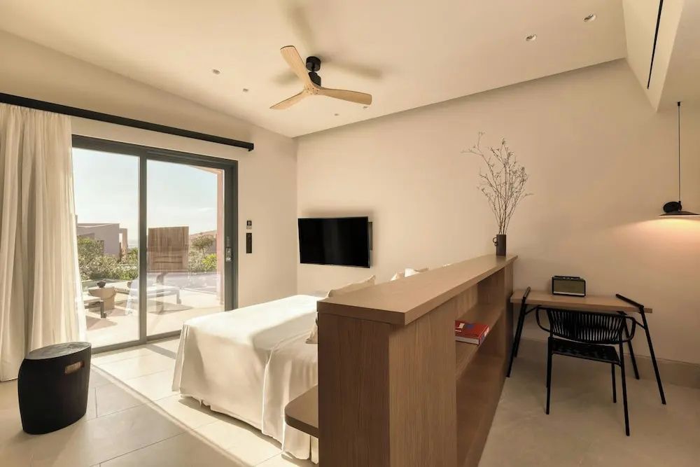 Modernes Hotelzimmer mit Doppelbett, Fernseher an der Wand und Blick auf die Terrasse.