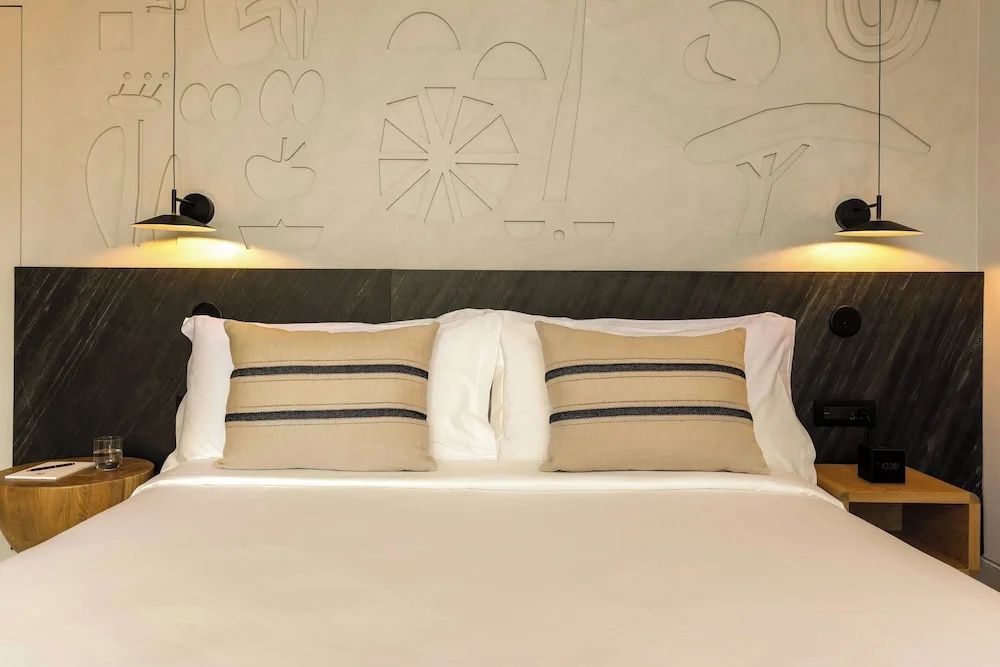 Doppelbett mit hellen Kissen und gestreiftem Muster vor einer gestalteten Wand.
