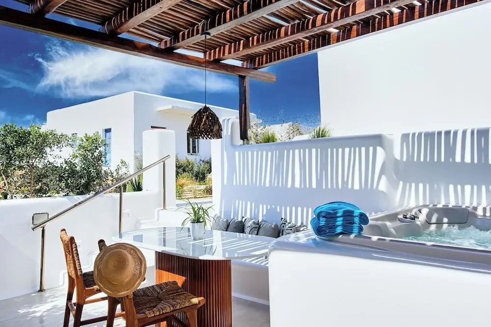 Überdachte Terrasse mit Sitzecke, Esstisch und Whirlpool unter einem Holzgebälk am Tag.