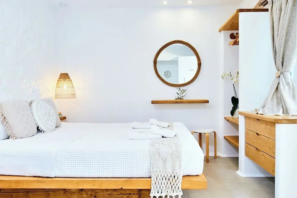Helles Hotelzimmer mit Doppelbett, hölzernem Wandregal und rundem Spiegel an weißer Wand.