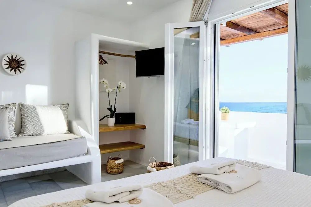 Blick aus dem weiß gestalteten Zimmer durch die offene Balkontür auf das blaue Meer.