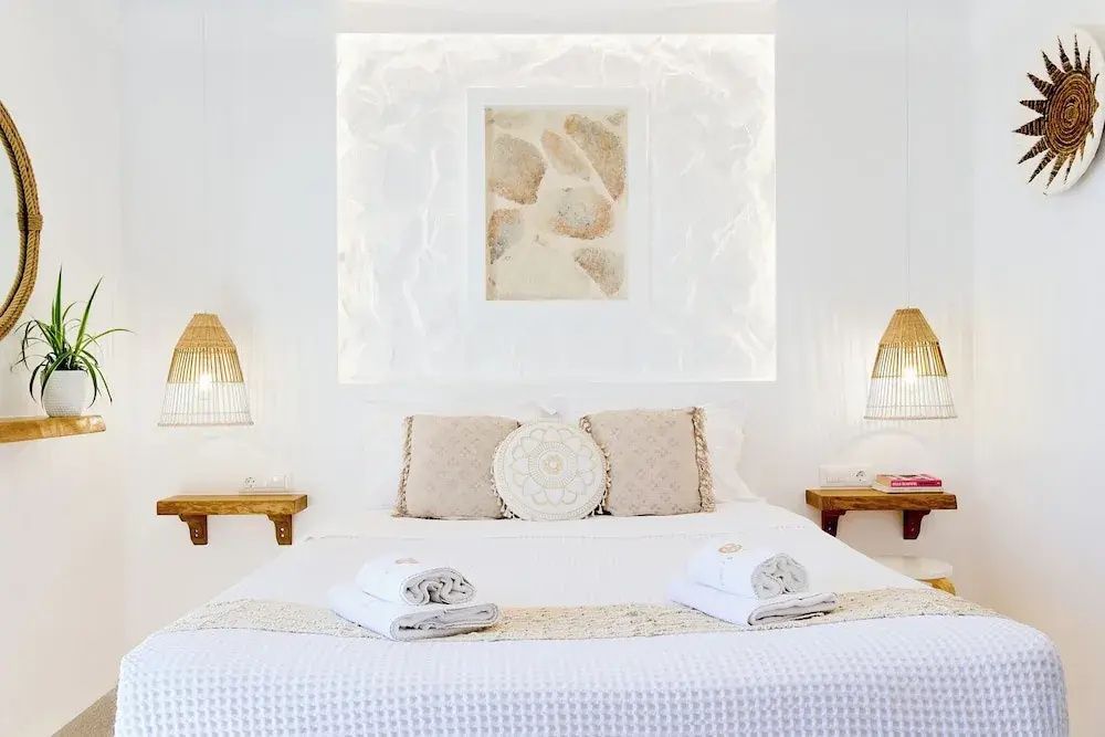 Weißes Doppelbett mit beigen Kissen und Dekoration an der hellen Wand.