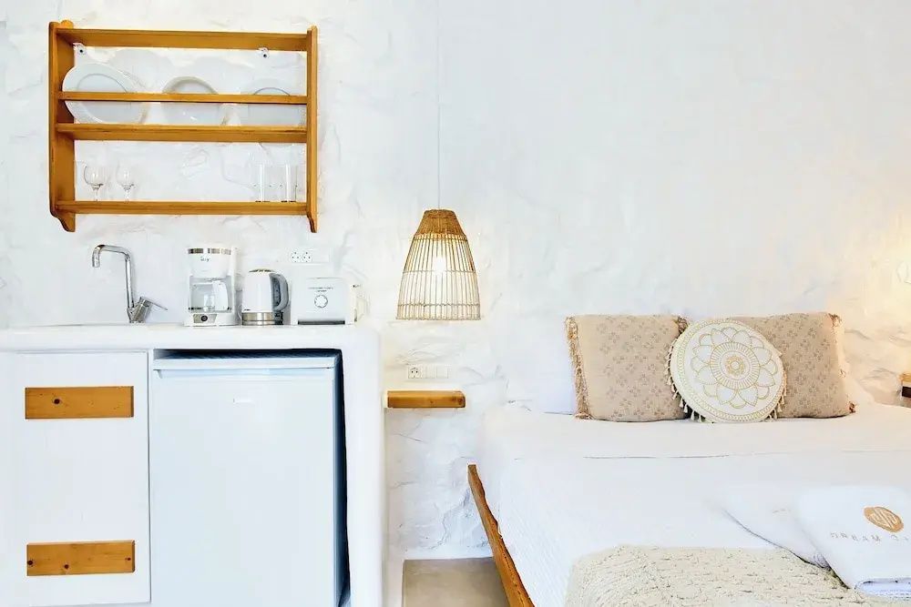 Zimmerbereich mit Minibar, Kaffeemaschine, Bett und einer Lampe aus Geflecht.