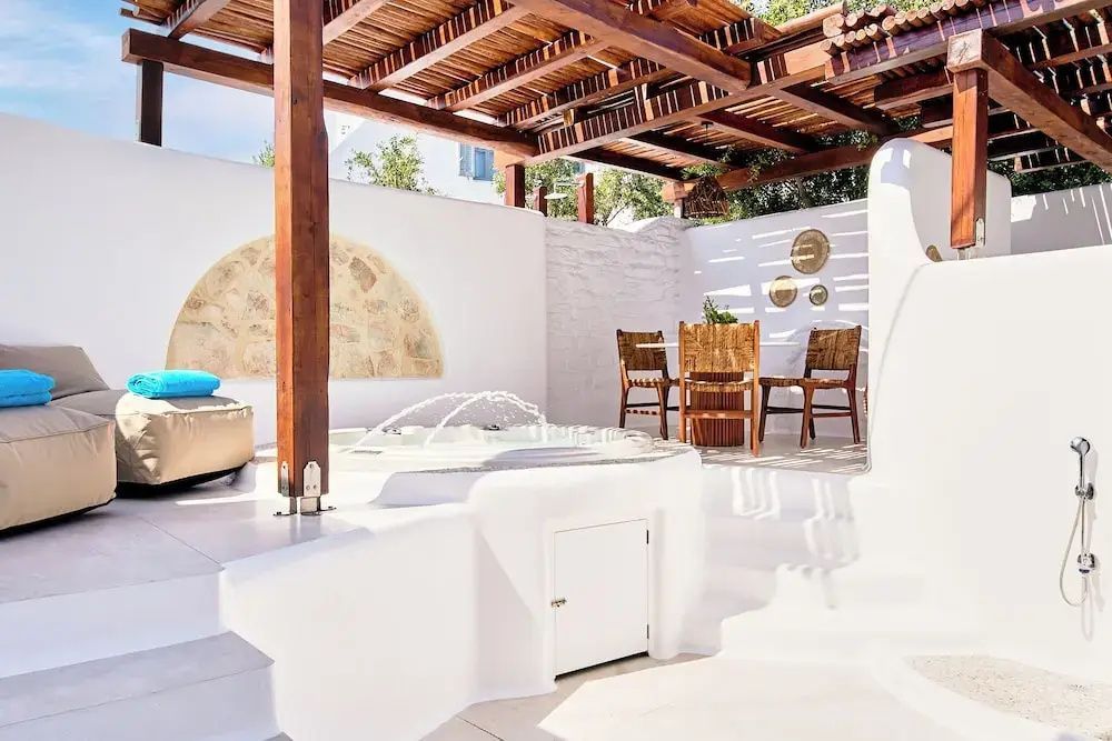 Sonnige Terrasse mit Holzpergola, Sitzgruppe und einem kleinen Pool mit Fontäne.