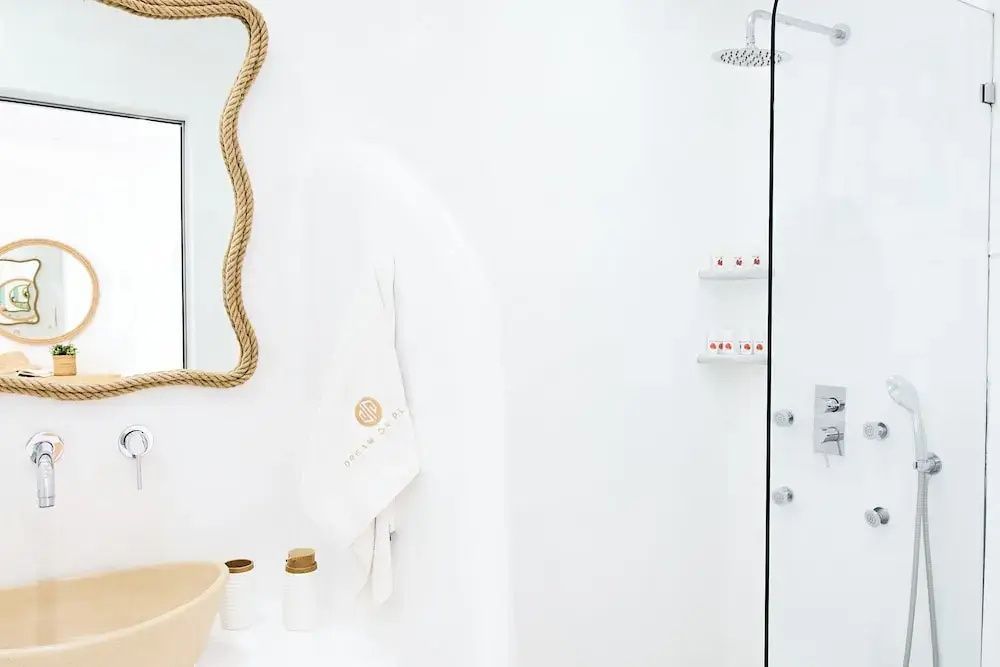 Weißes Badezimmer mit ebenerdiger Dusche, Seilspiegel und Waschtisch.