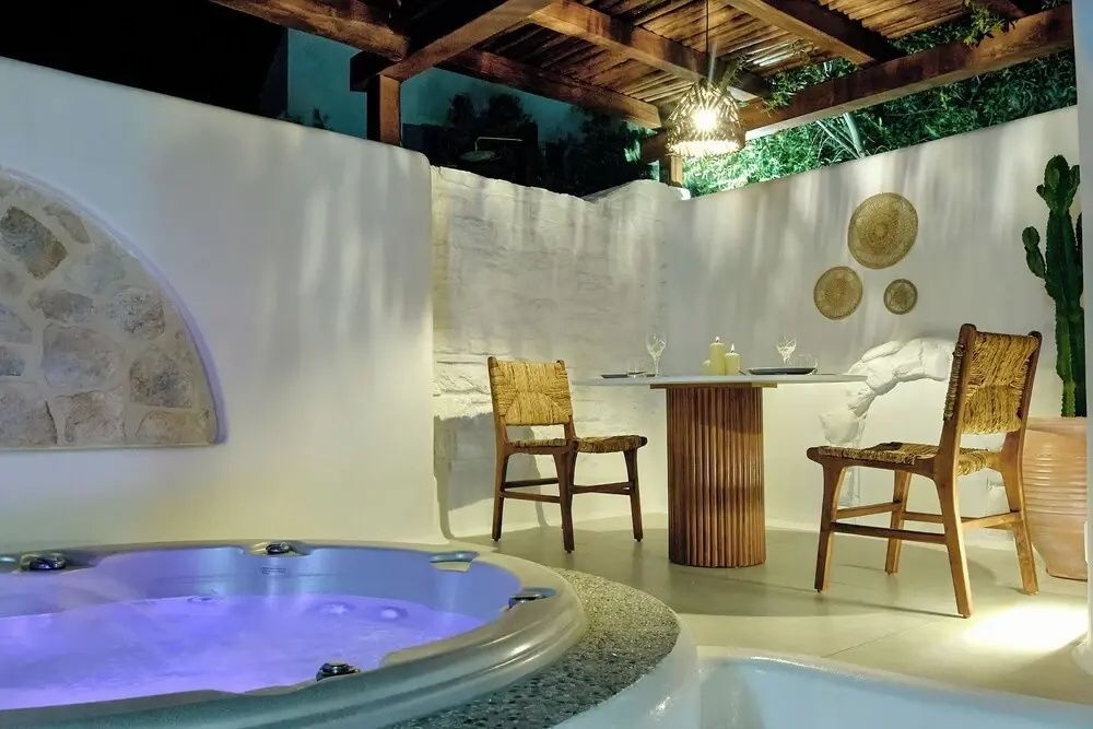 Beleuchteter Whirlpool auf einer überdachten Terrasse mit Esstisch und Stühlen bei Nacht.