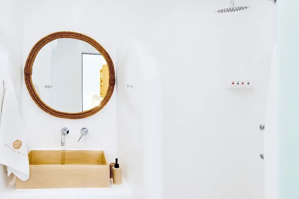 Weißes Badezimmer mit rechteckigem Holzwaschbecken, rundem Spiegel und Duschbereich.