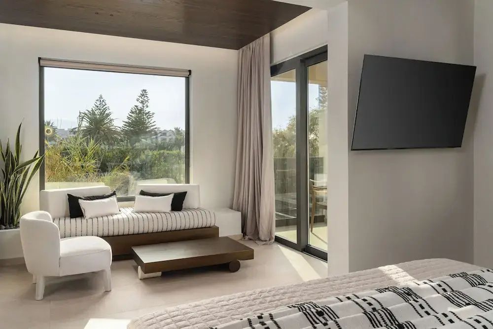 Heller Wohnbereich einer Suite mit gestreiftem Daybed, Couchtisch und Fernseher an der Wand.