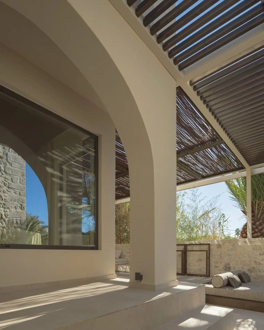 Überdachte Terrasse mit Rundbögen, Holzpergola und Blick auf eine Natursteinmauer.