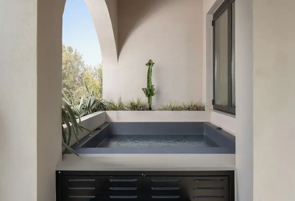 Ein kleiner rechteckiger Pool auf einer überdachten Terrasse mit Pflanzen im Hintergrund.