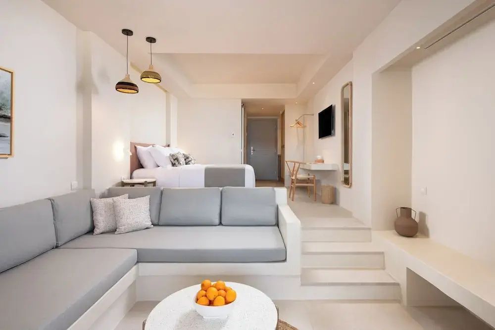 Helles Zimmer mit grauer Sitzecke im Vordergrund und erhöhtem Doppelbett im Hintergrund.