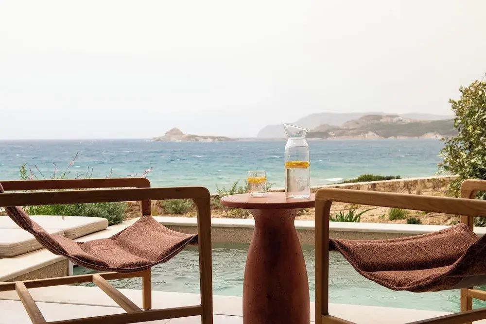 Terrasse mit zwei Holzstühlen, einem Tisch und Blick auf das Meer und die gegenüberliegende Küste.