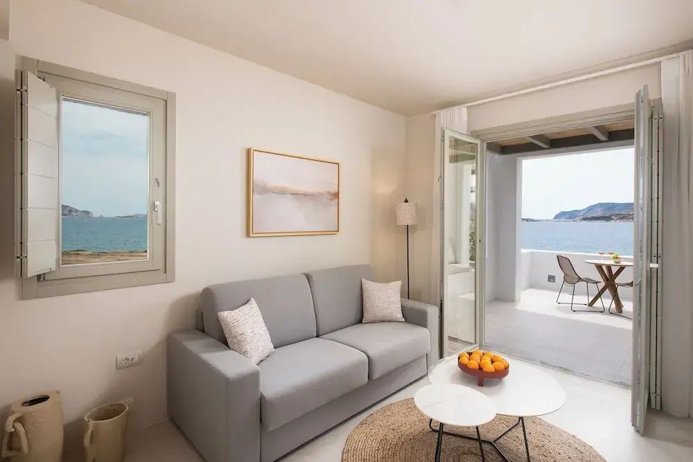 Helles Wohnzimmer einer Suite mit grauem Sofa, Couchtischen und Zugang zur Balkonterrasse mit Meerblick.