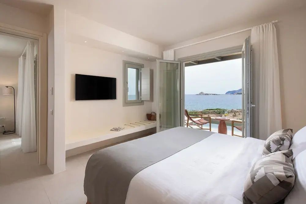 Schlafzimmer mit Doppelbett, Wandfernseher und geöffneter Terrassentür mit direktem Blick auf das Meer.