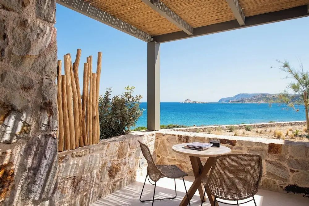 Überdachte Terrasse mit Holzpergola, Steinmauer, Sitzgruppe und Blick auf das blaue Meer.