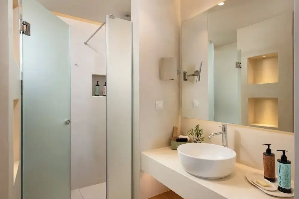 Modernes Badezimmer mit weißem Aufsatzwaschbecken, großem Spiegel und einer Dusche.