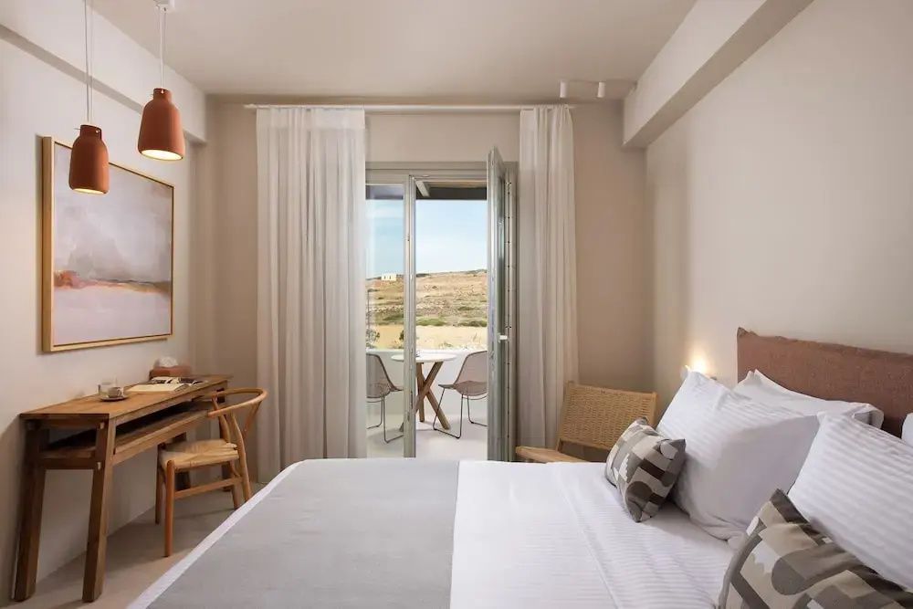 Schlafbereich mit Doppelbett und geöffnete Balkontür mit Blick auf die Landschaft.