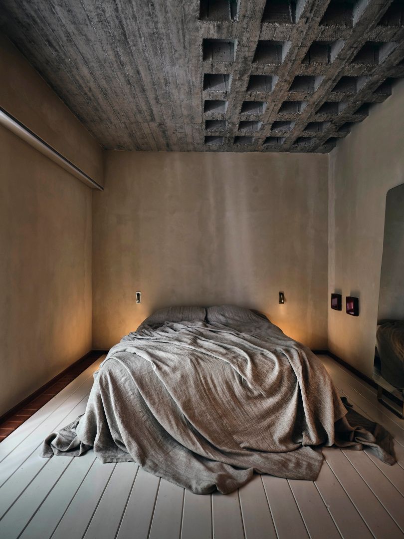 Minimalistisches Schlafzimmer mit Sichtbetondecke und Bett mit naturfarbener Bettwäsche.