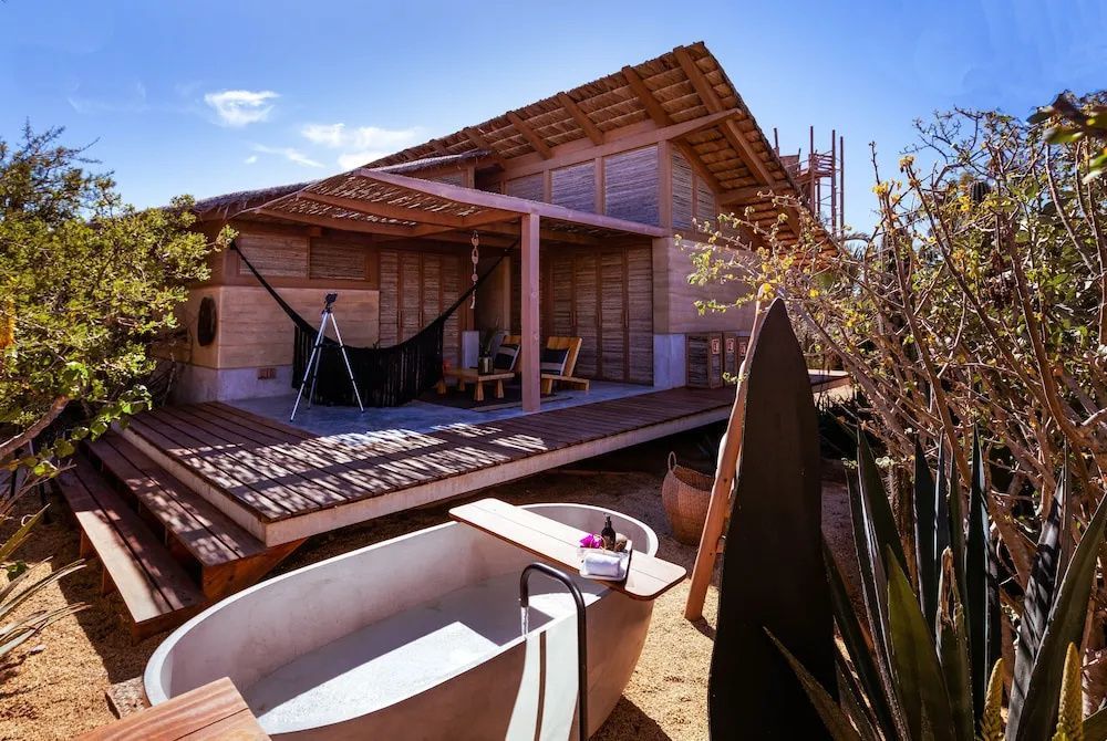 Holzterrasse eines Bungalows mit Hängematte und freistehender Badewanne im Außenbereich.