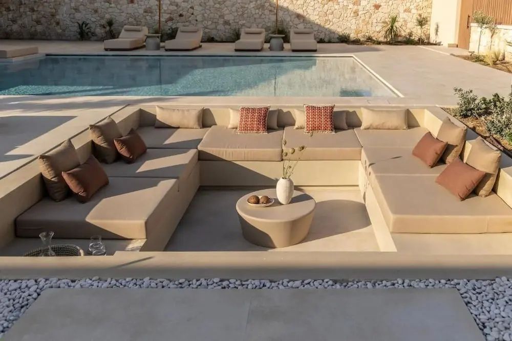 Eingelassener Loungebereich mit beigen Polstern im Außenbereich neben dem Pool.