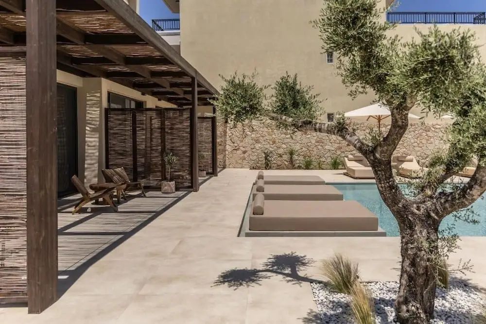 Poolanlage mit gepolsterten Sonnenliegen am Beckenrand und überdachter Terrasse.