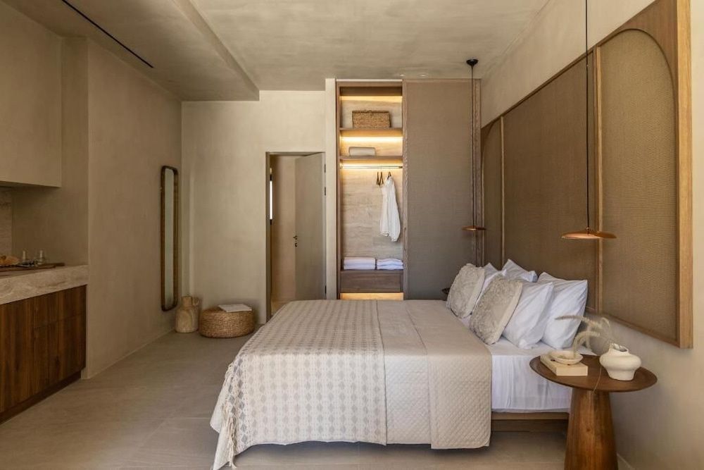 Schlafbereich einer Suite mit Doppelbett in Erdtönen, offenem Kleiderschrank und Spiegel.