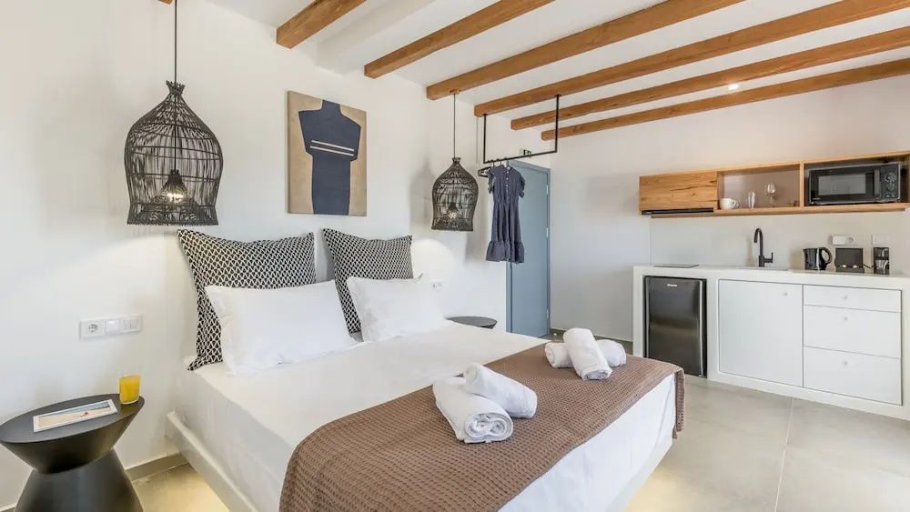 Doppelbett mit weißer Bettwäsche, brauner Tagesdecke und Holzbalken an der Decke.