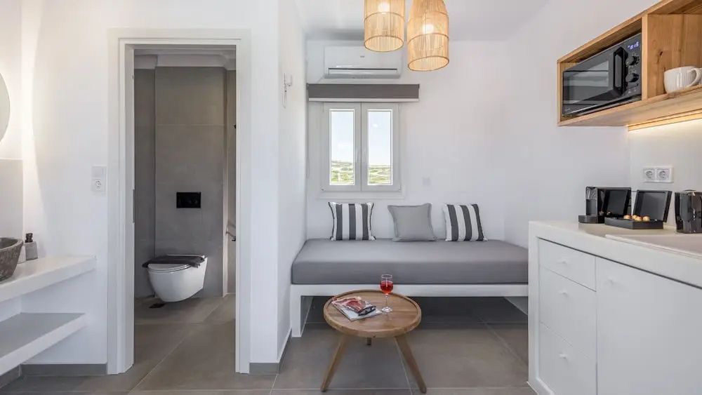 Sitzbereich mit grauem Tagesbett, kleinem Holzcouchtisch und Blick ins Badezimmer.