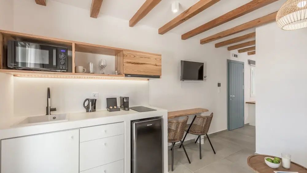 Wohnbereich mit Holzbalkendecke, Fernseher an der Wand und Küchenzeile.