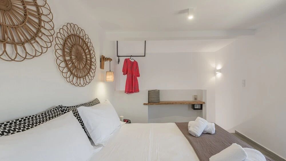Doppelbett mit weißen Kissen, gefalteten Handtüchern und Flechtdekoration an der Wand