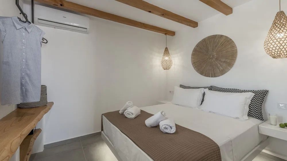 Schlafzimmer mit weiß gedecktem Doppelbett, Holzdeckenbalken und Weidenlampe.