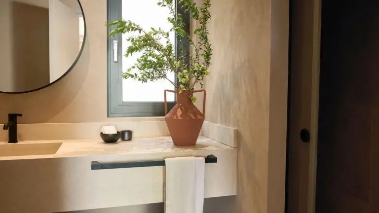 Waschtisch aus Naturstein mit einer rustikalen Vase, Pflanzenzweigen und Handtuchhalter.