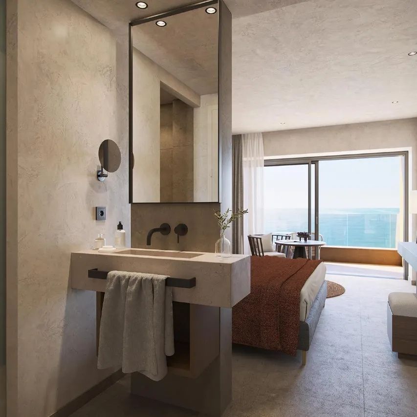 Waschtisch mit freistehendem Spiegel und Blick durch das Zimmer auf den Balkon mit Meerblick.