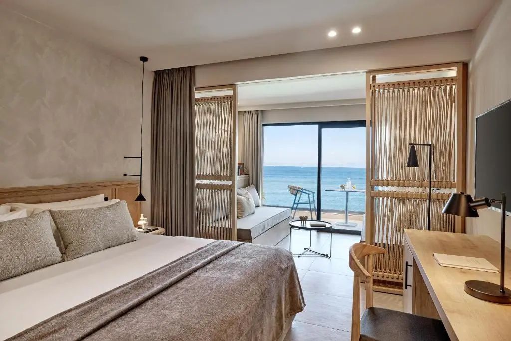Helles Hotelzimmer mit Doppelbett, Raumteilern aus Holz und Balkon mit Blick auf das Meer.