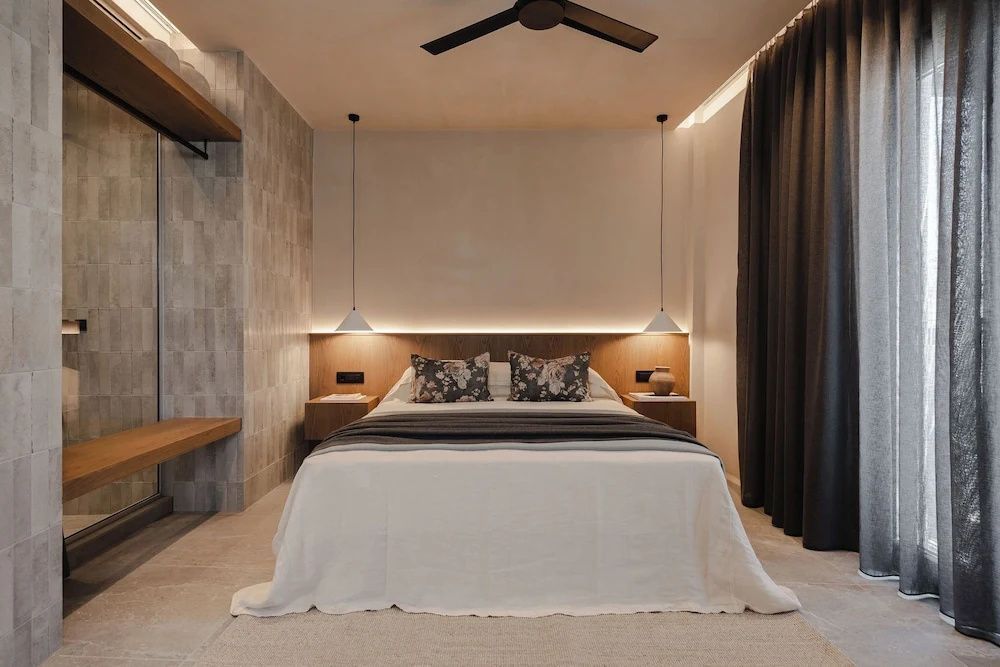 Doppelbett mit Kissen und Decke vor einer Holzwand mit indirekter Beleuchtung.
