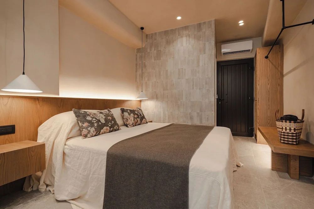 Helles Hotelzimmer mit Doppelbett und Fliesenwand sowie dunkler Eingangstür