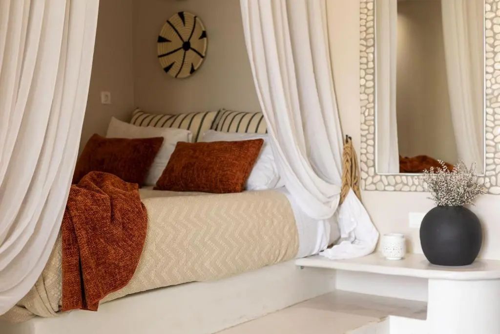 Bettnische im Zimmer mit hellen Stoffvorhängen, gestreifter Bettwäsche und Kissen.