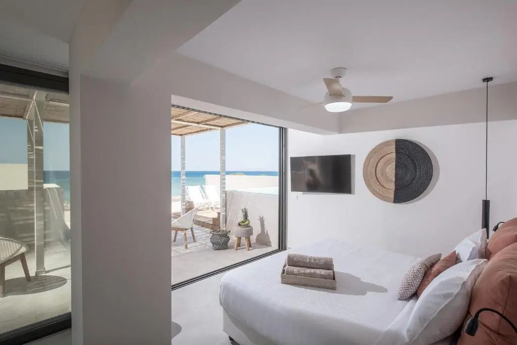 Helles Hotelzimmer mit Doppelbett, Deckenventilator und Schiebetür zur Terrasse mit Meerblick.