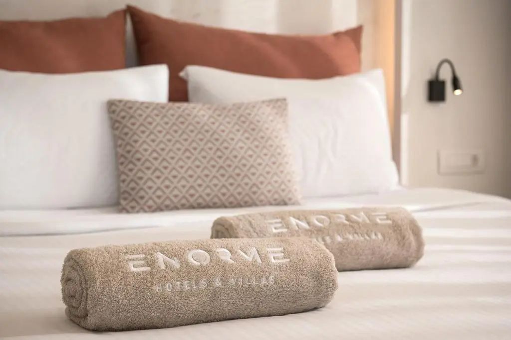 Zwei braune, eingerollte Handtücher mit Namensstickerei liegen auf einem Bett mit weichen Kissen.