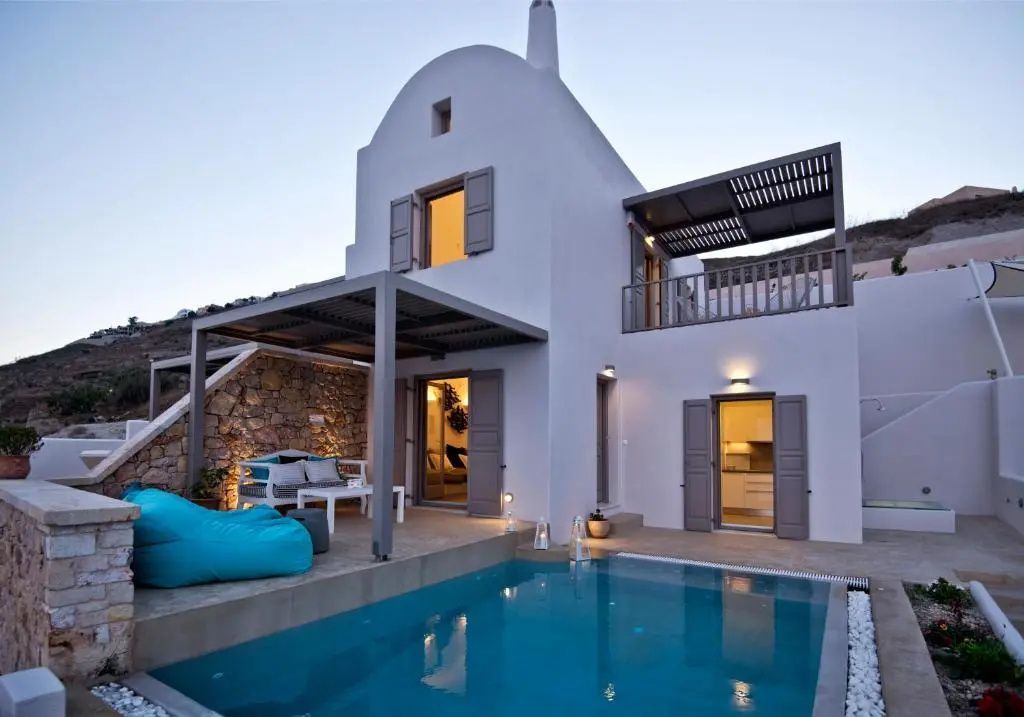 Weiße Villa im kykladischen Stil bei Dämmerung mit einem beleuchteten Pool und Terrasse.