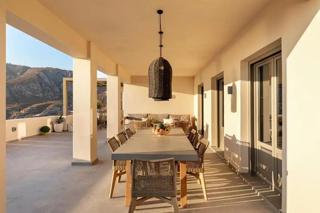Überdachte Terrasse mit langem Esstisch, Stühlen und einer hängenden Lampe bei Sonnenlicht.