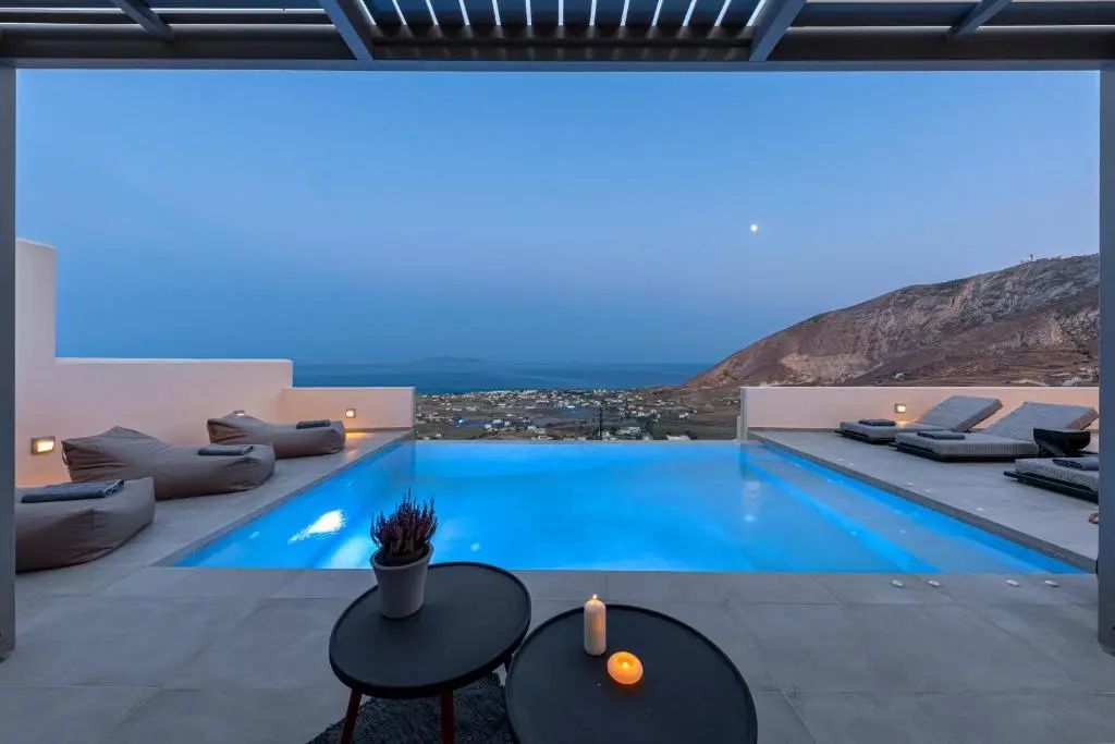 Beleuchteter Infinitypool auf einer Terrasse mit Blick auf die Küste bei Dämmerung.
