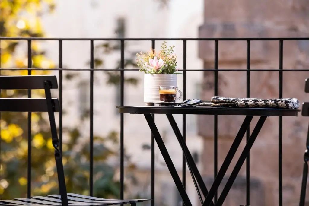 Schwarzer Bistrotisch mit Espresso, Sonnenbrille und Blumen auf einem Balkon.