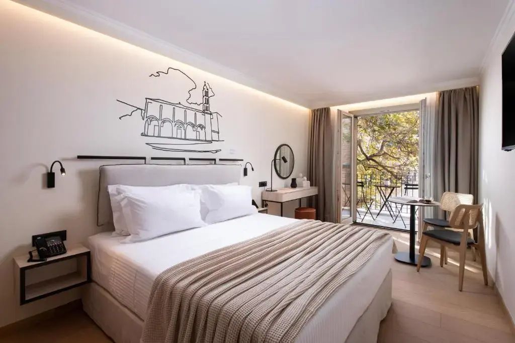 Helles Hotelzimmer mit Doppelbett, Wandzeichnung und geöffneter Balkontür mit Blick ins Grüne.
