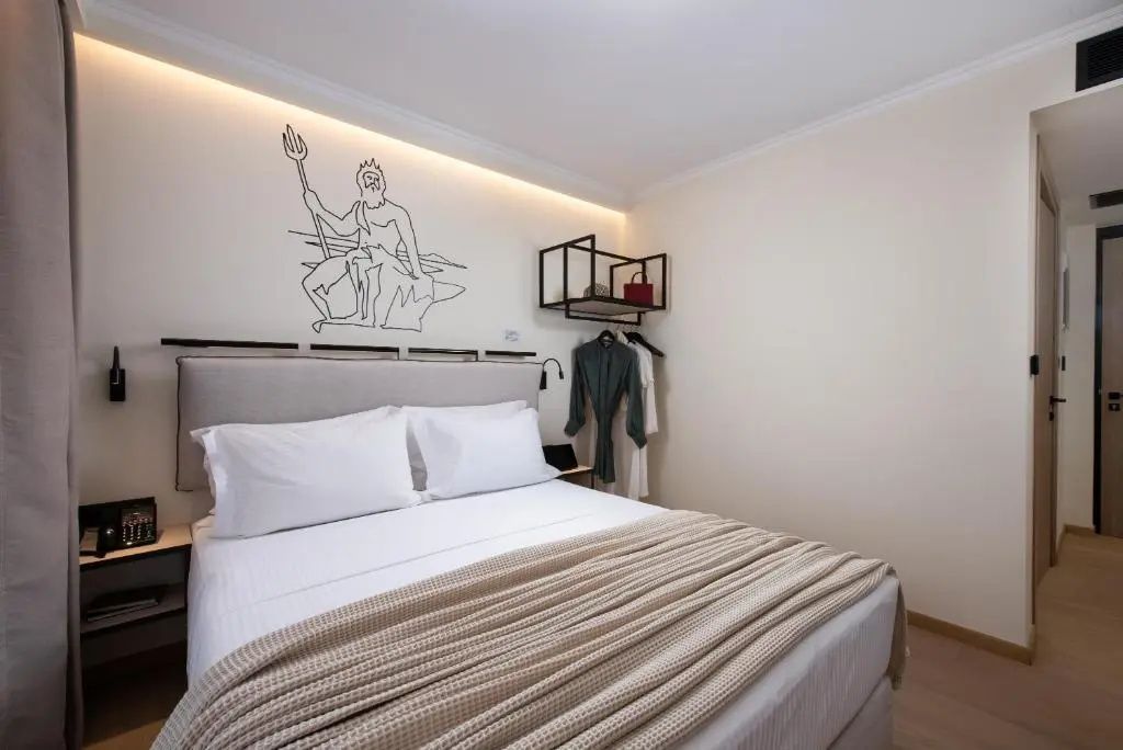 Doppelbett mit weißer Bettwäsche, beigefarbener Tagesdecke und Grafik an der Wand.