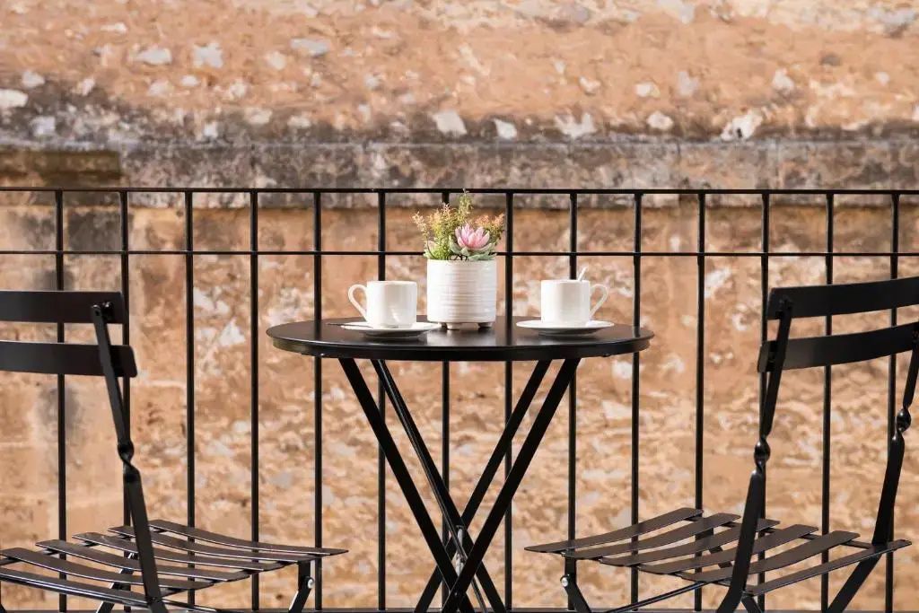 Kleine Sitzgruppe auf dem Balkon mit schwarzem Tisch, Kaffeetassen und Stühlen