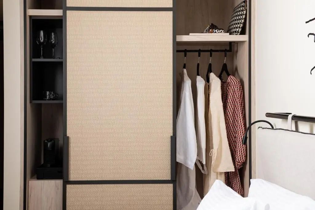 Eingebauter Kleiderschrank aus Holz mit geflochtener Tür und aufgehängter Kleidung.