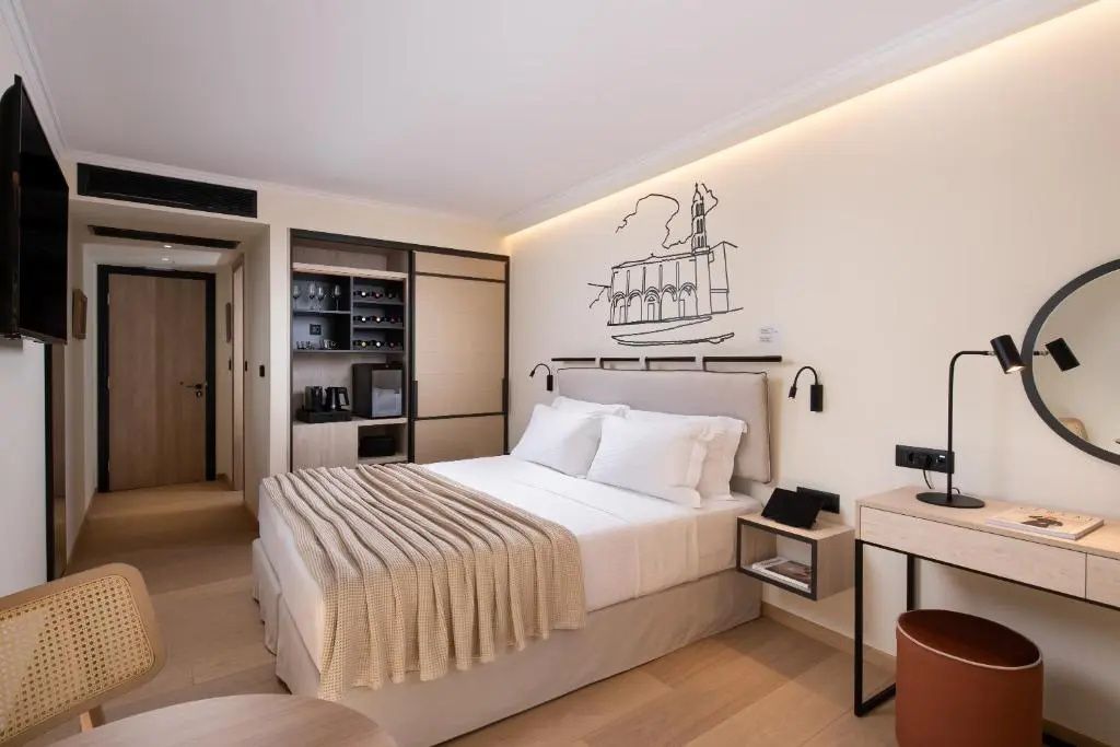 Modernes Hotelzimmer mit Doppelbett, Wandschrank, Minibar und kleiner Wandzeichnung.