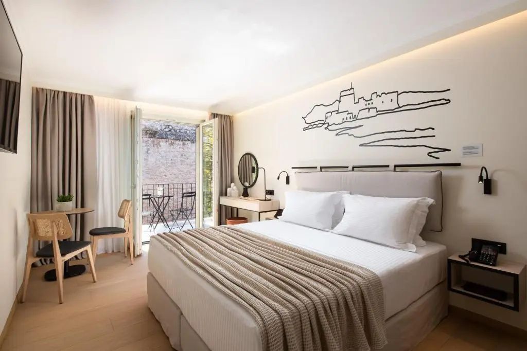 Doppelzimmer im Hotel mit hellem Bett, Stuhl am Balkon und dekorativer Wandgrafik.