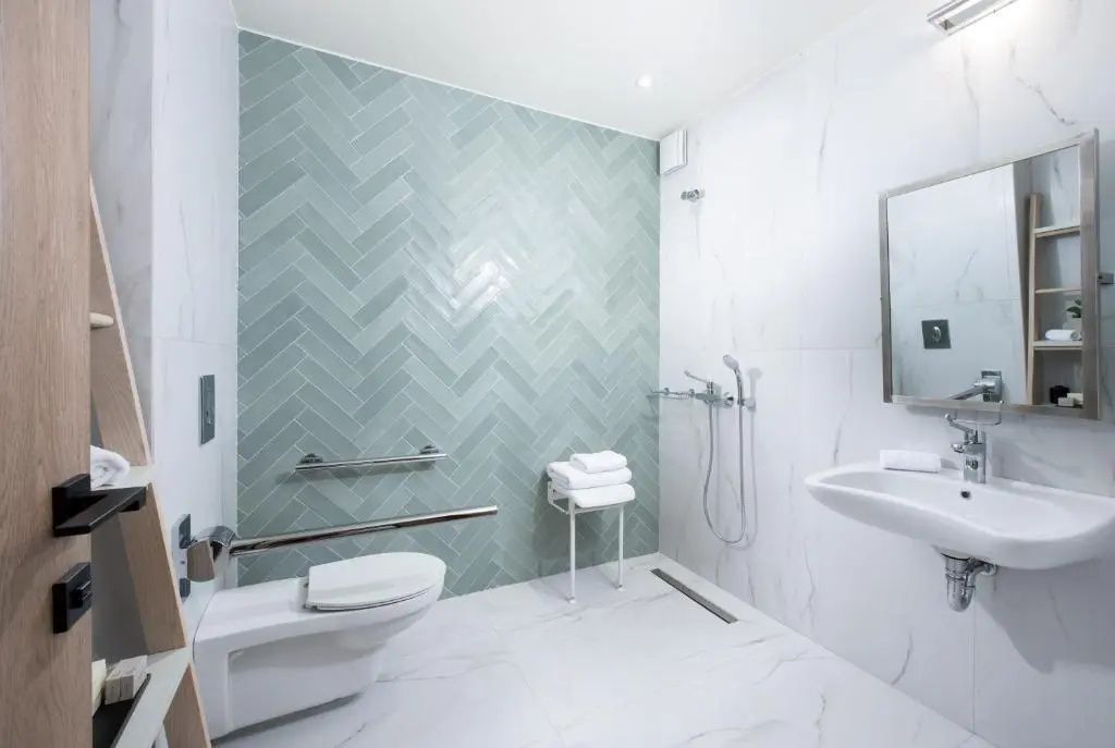 Barrierefreies Badezimmer mit blaugrüner Fliesenwand, Dusche, Haltegriffen und WC.